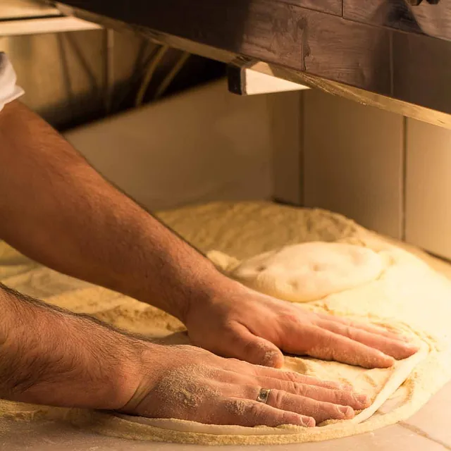 Hender som kveiler ut pizzadeig.