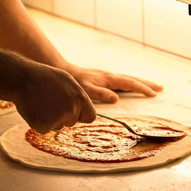 Tomatsaus smøres på pizzabunn.